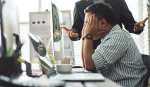 Man at work stressed out as another man stands over him